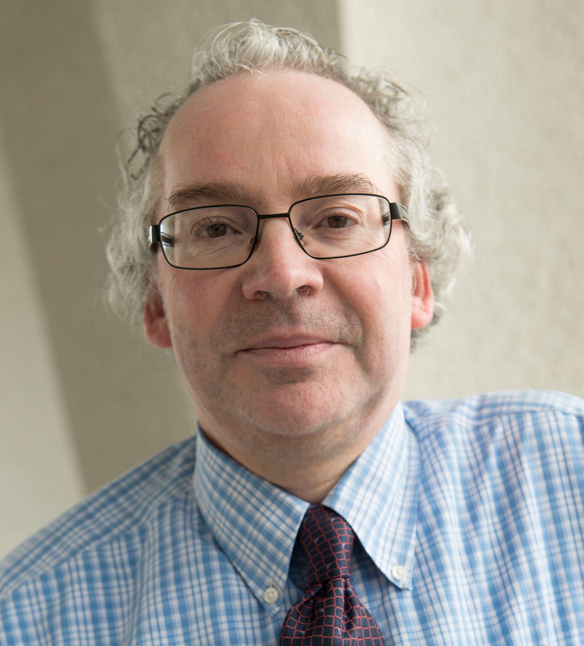 Portrait photo of Stefan, a white man in glasses with greying hair, glasses, wry smile, formal shirt and tie