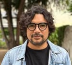 Picture of Alberto, a man with light brown skin, black flowing hair and a goatee. He has black glasses and a denim jacket.
