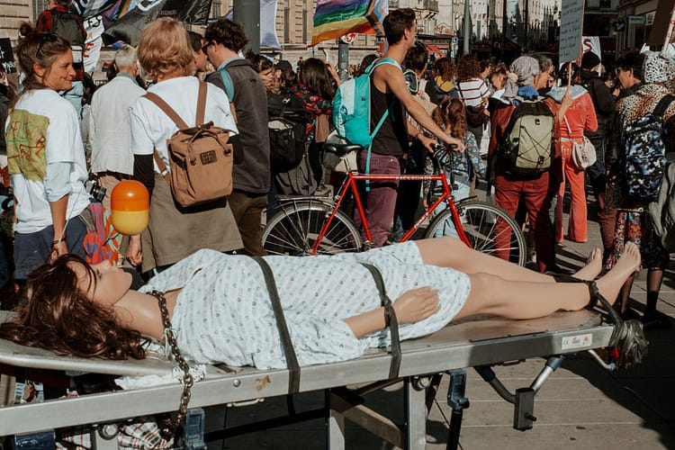 A photo of a female mannequin who is strapped to a stretcher and wearing a hospital gown, at a protest.